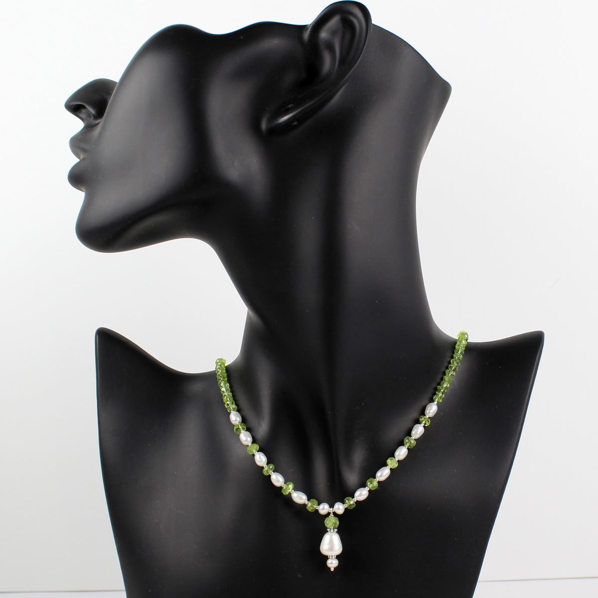 A beaded necklace with white pearls and green beads, featuring a teardrop-shaped white pearl pendant, displayed on a black mannequin bust against a white background.