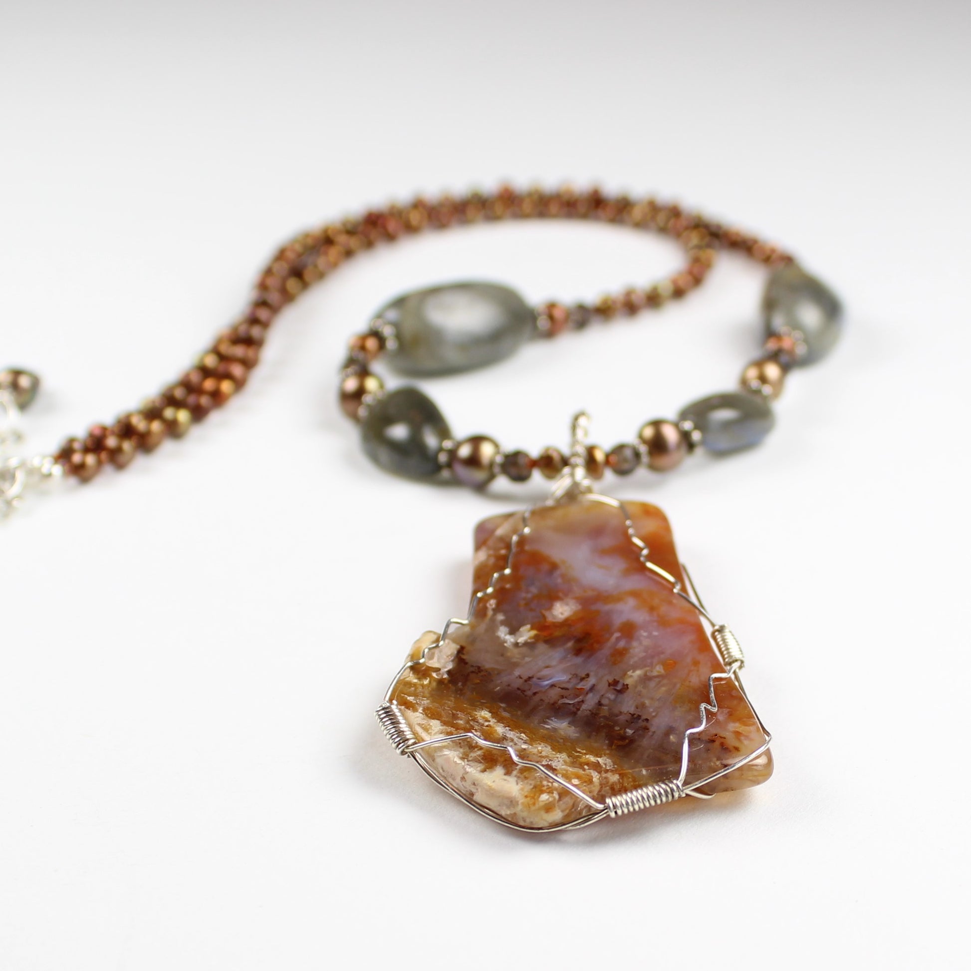 Brown and red agate slice wrapped in sterling silver wire hangs from 21 inch long string of copper pearls and labradorite stones.